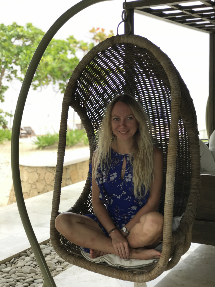 Olga seated in a woven hanging chair beside the beach