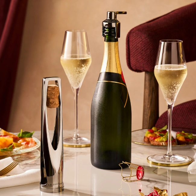 A crown sealer fitted to a sparkling-wine bottle beside two filled flutes on a table.