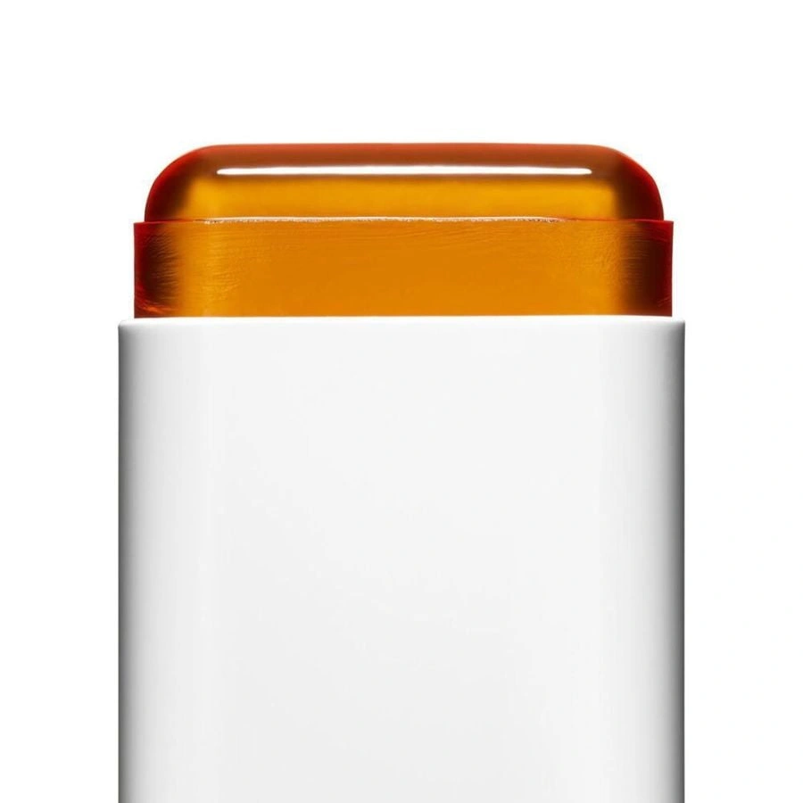 Close-up of the amber sunscreen stick extended above its white case.