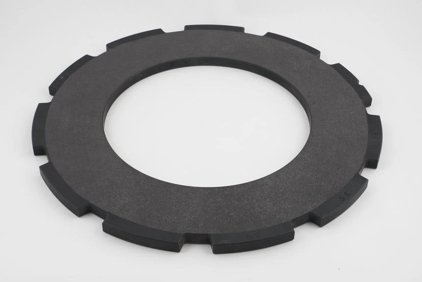 Dark circular carbon brake disc made for Concorde, with evenly spaced rectangular lugs around its outer edge.
