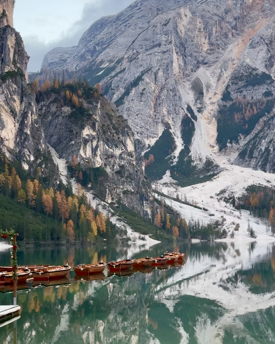 Wooden rowing boats beneath pale rock walls and autumn larches at Lago di Braies.