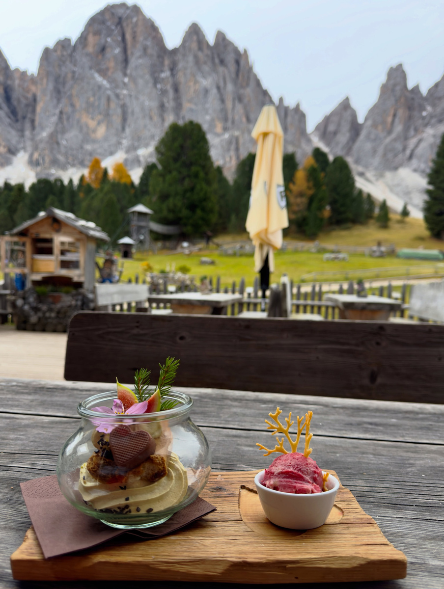 A dessert in a round glass and a scoop of berry-coloured ice cream on the wooden terrace at Geisleralm.