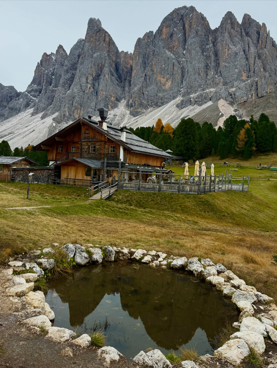 Geisleralm beneath the Odle peaks, reflected in a small stone-edged pool.