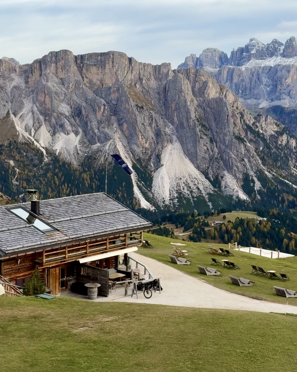 A wooden mountain hut and its terrace beneath towering pale limestone cliffs.