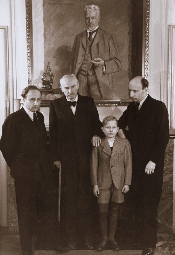 Three men and a boy from the Leitz family stand beneath a large painted portrait of Ernst Leitz I.