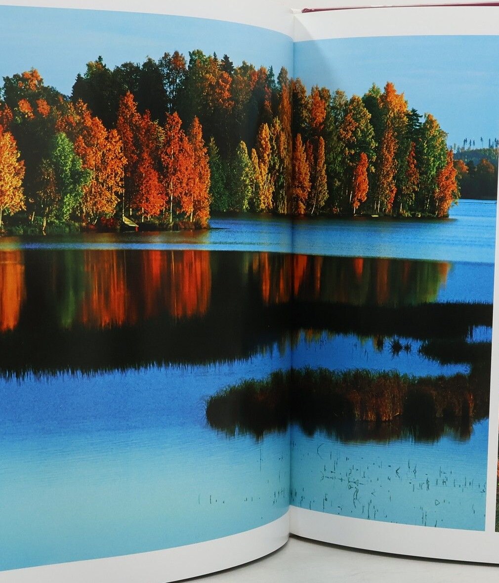 An open spread of a Finnish lake with orange and green autumn trees reflected in still blue water.
