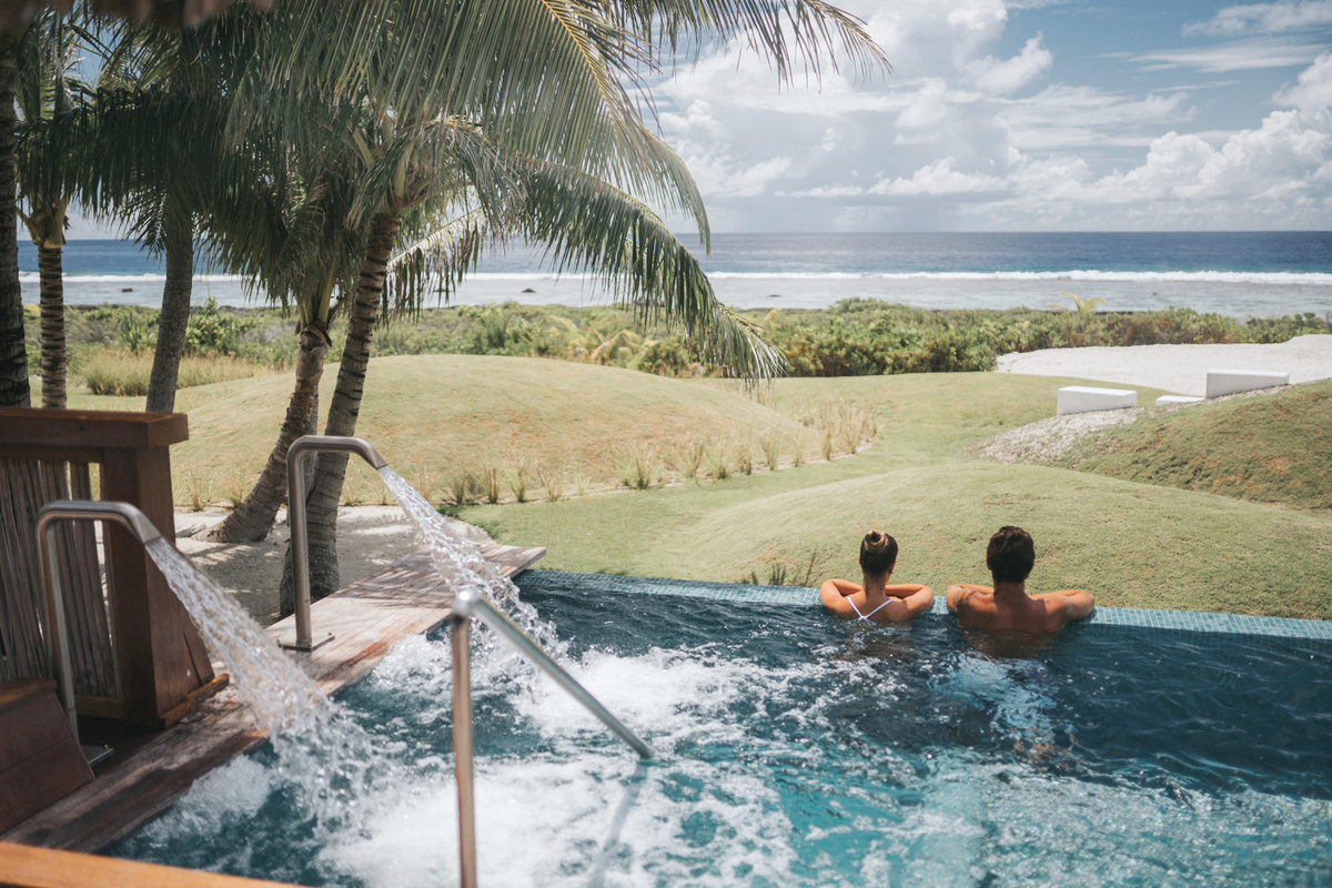 Two guests in the spa vitality pool overlooking palm trees and the Pacific Ocean at Four Seasons Bora Bora