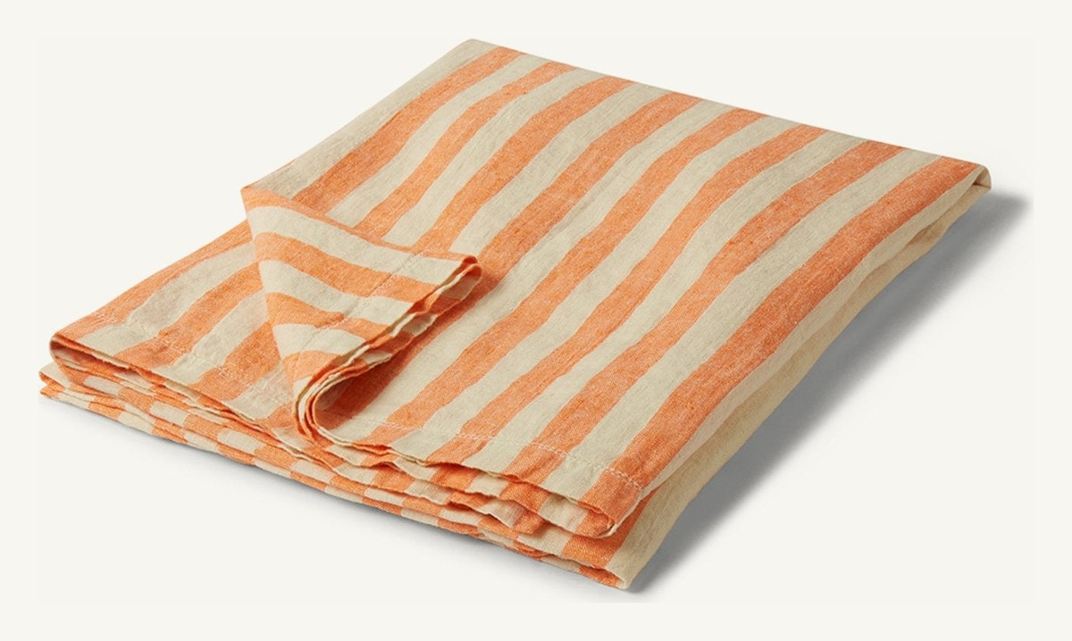 Folded Frescobol Carioca linen beach towel with orange and off-white stripes.