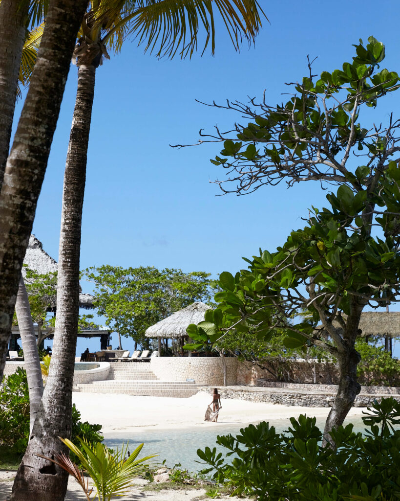 A woman walking along GoldenEye’s sandy beach, seen through palms and tropical foliage.