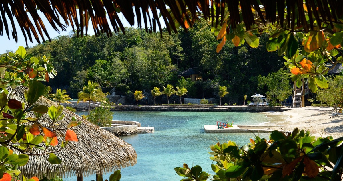 A sheltered cove and sandy beach at GoldenEye, framed by thatch and tropical foliage.