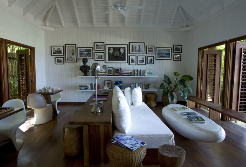 The Fleming Villa’s white timber living room, with books, framed photographs, open wooden shutters and a white sofa.