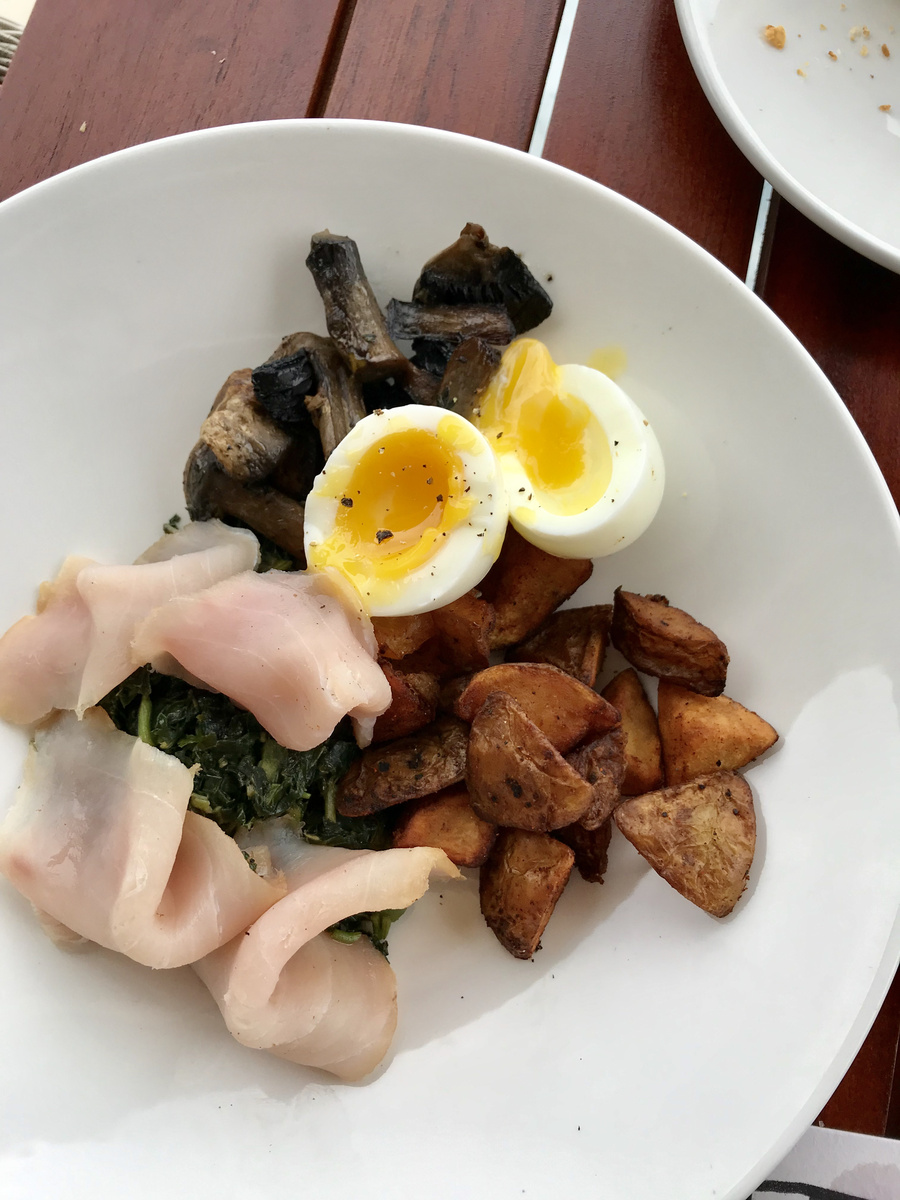 Smoked marlin, callaloo, soft-boiled eggs, mushrooms and potatoes on a white plate.