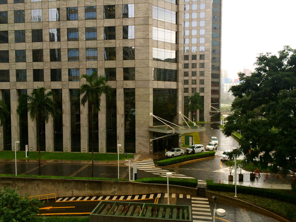 Rain over granite-clad office towers, palms and a driveway lined with white taxis in São Paulo’s Berrini district.