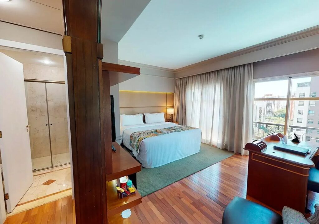 A Collection room with wooden floors, a queen bed, an armchair and a glass door to a small balcony.
