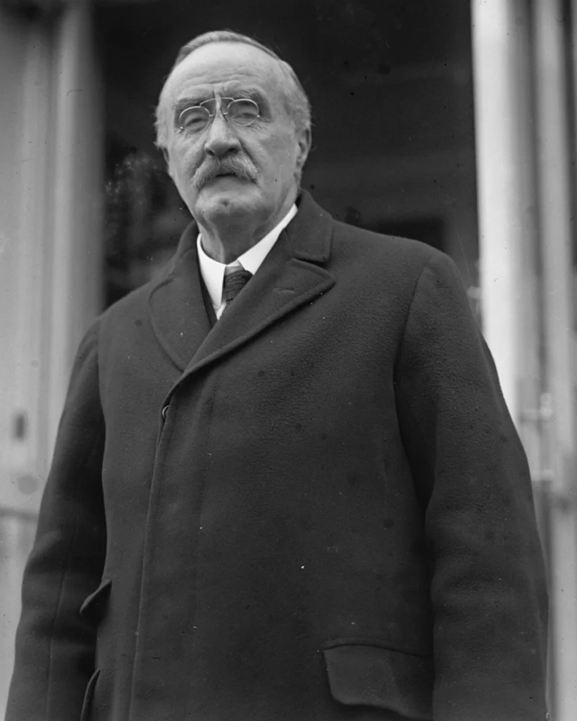 Henry Lunn wearing pince-nez, a moustache and a dark overcoat, standing outside the White House.