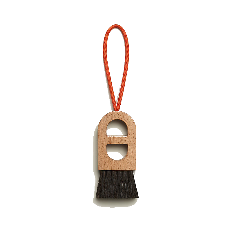 Hermès wooden beach brush with an orange wrist cord and dark bristles.