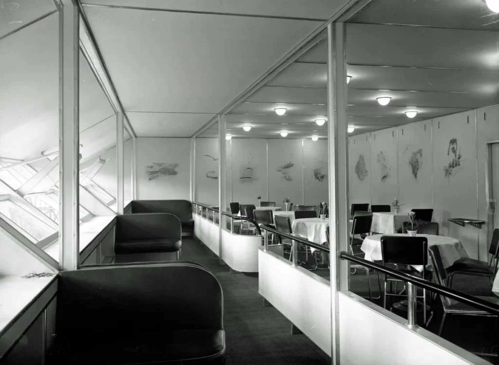 Black-and-white photograph of Hindenburg's windowed promenade beside a dining room set with white tablecloths and tubular chairs.