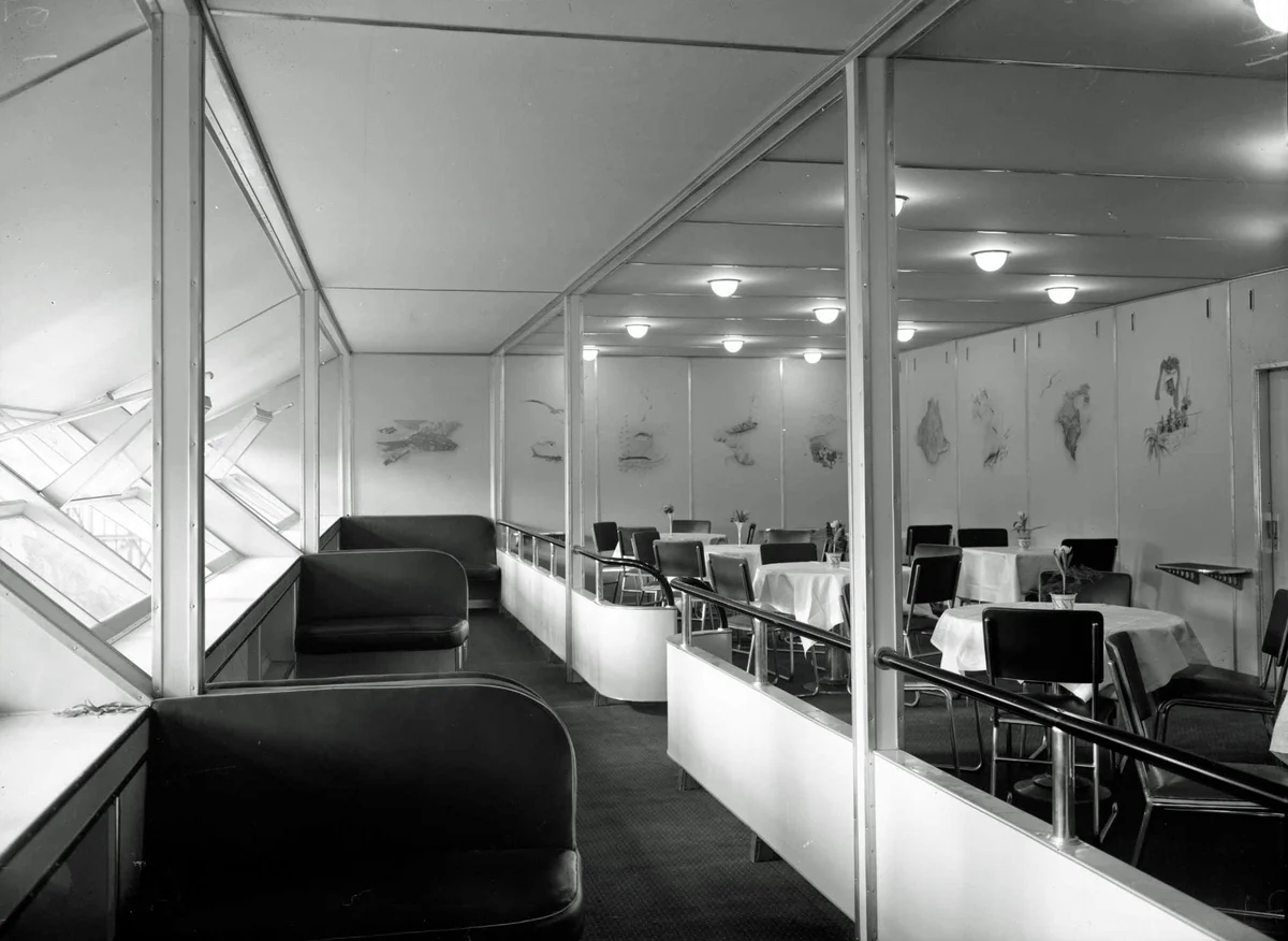 Black-and-white photograph of Hindenburg's windowed promenade beside a dining room set with white tablecloths and tubular chairs.