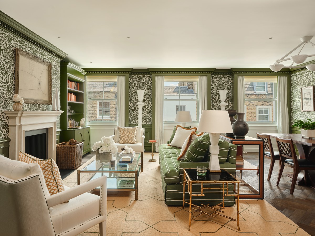 A green-panelled suite living room with a stack of books on a glass coffee table, a fireplace, bookshelves and a striped green sofa.