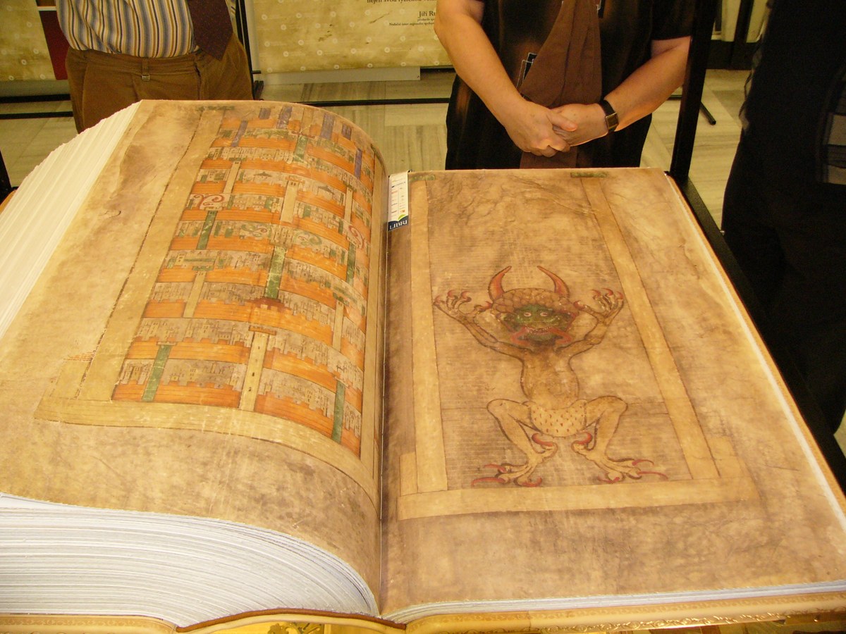 A full-size facsimile of the Codex Gigas lies open on a table, showing the page with the Devil beside a page of text.