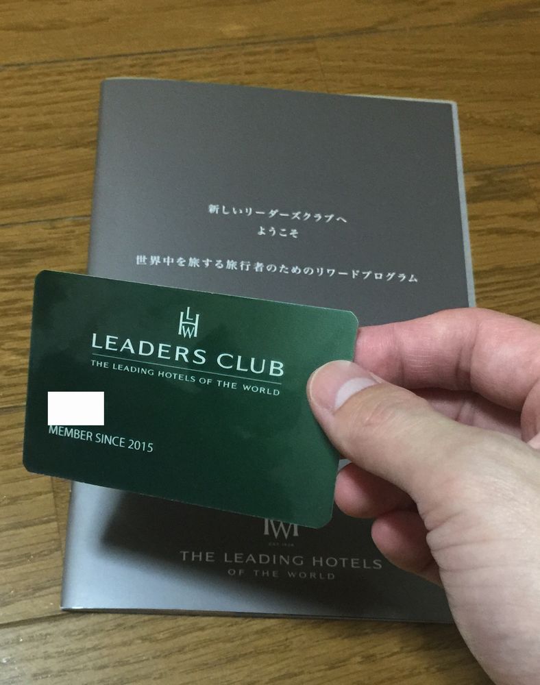 A hand holds a green Leaders Club membership card above its welcome booklet.