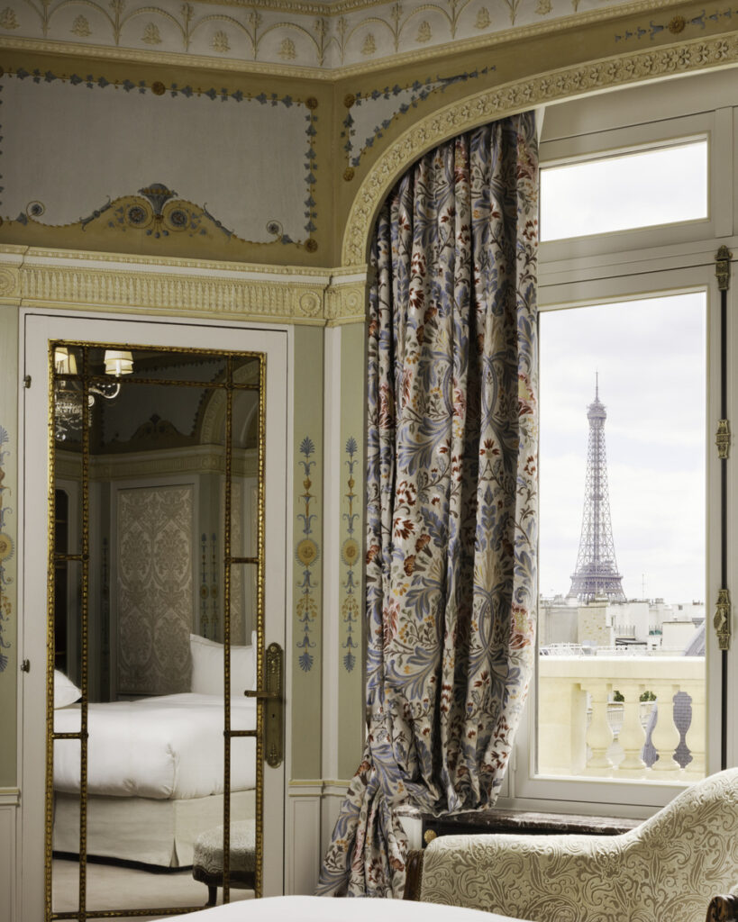 The Eiffel Tower framed by a window beside a gilded mirror in a Hôtel Raphael suite.