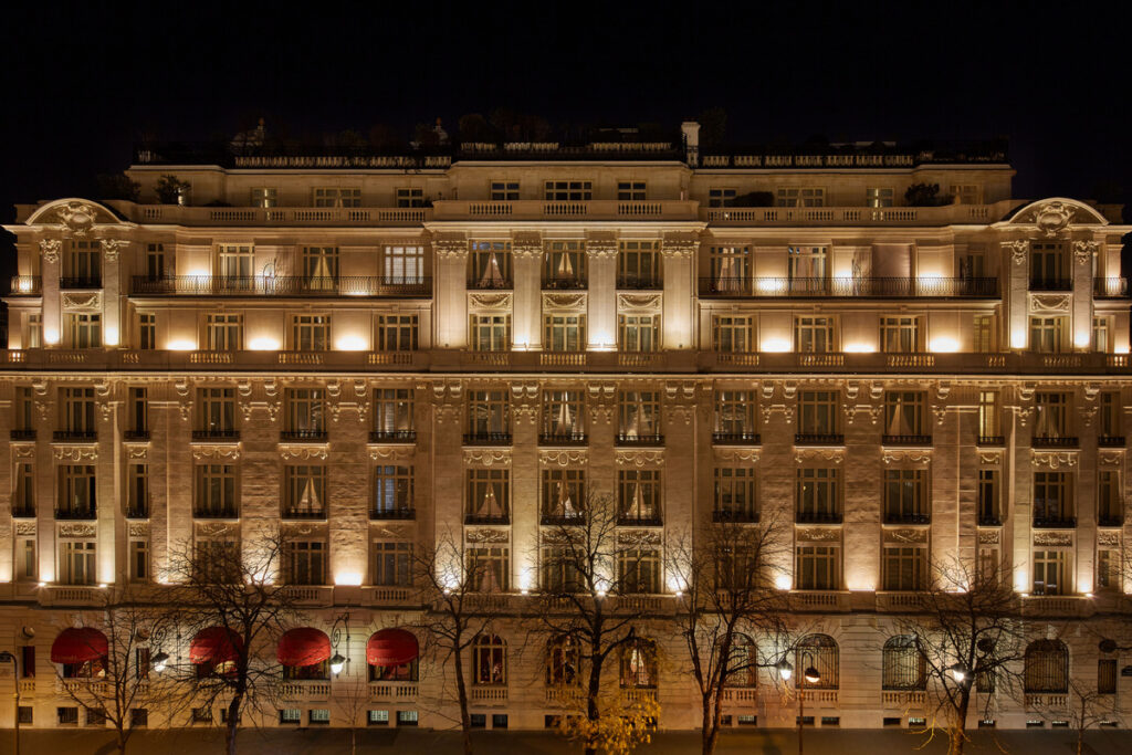 The illuminated stone façade of Hôtel Raphael at night, with red awnings over the entrance.
