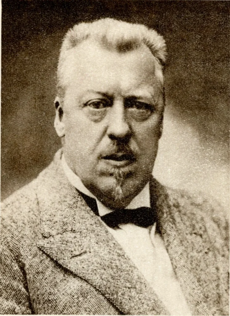 Black-and-white portrait of Hugo Eckener with brushed-back hair, heavy lower eyelids, a moustache and pointed goatee, wearing a tweed jacket and bow tie.