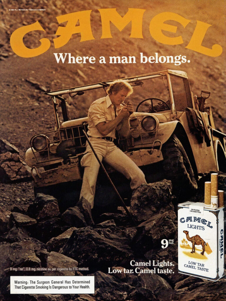 1983 Camel advertisement showing a man lighting a cigarette beside an open four-wheel-drive vehicle on rocky ground, beneath “Where a man belongs.”