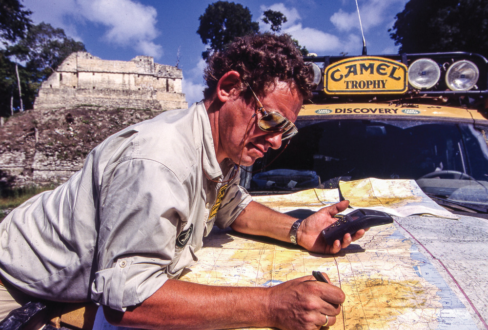 Iain Chapman uses a handheld GPS and writes on a paper map spread across a yellow Discovery’s bonnet.