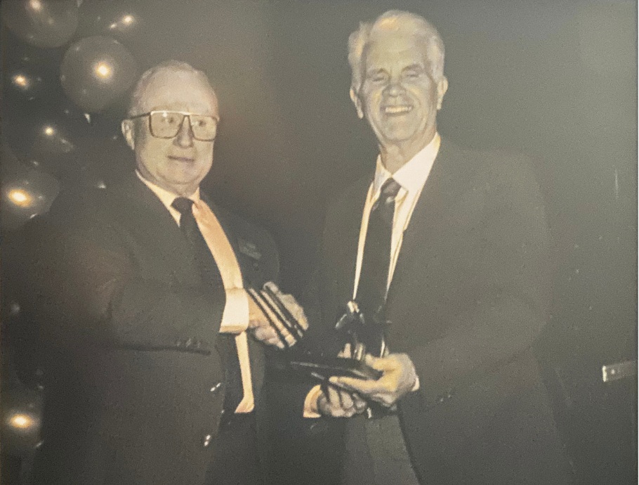 John Cronin, left, and Ralph Erickson in suits, holding an award.