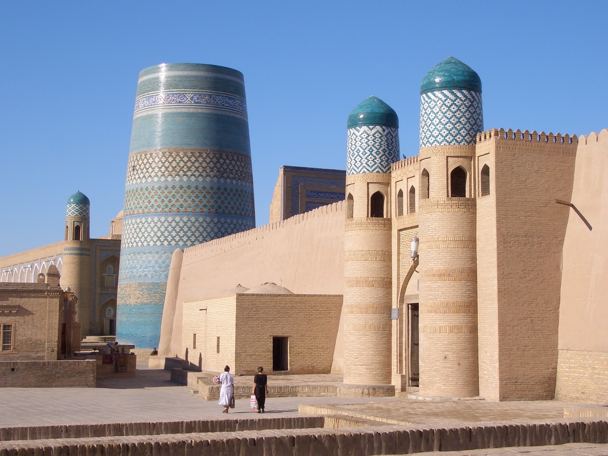 The turquoise Kalta Minor minaret beside the brick walls and twin towers of the western gate of Itchan Kala in Khiva.
