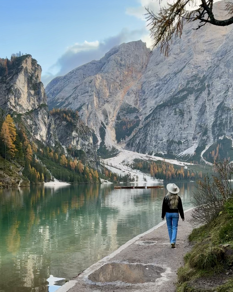 Olga walks beside Lago di Braies, with wooden boats and mountain reflections on the water.