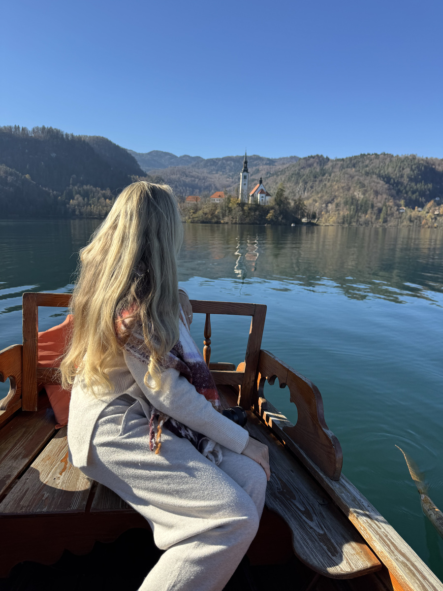 Olga looking towards Bled Island from a wooden rowing boat, with the seats and an oar visible.