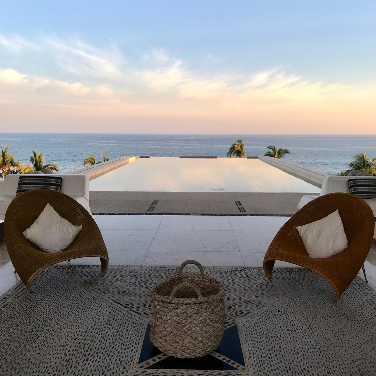 Woven chairs on a terrace facing the reflecting pool and the sea.
