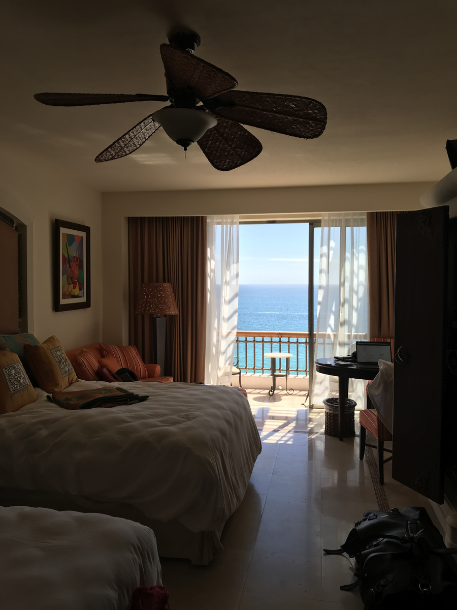 The room at Marquis Los Cabos with two beds, a sitting area and open balcony doors facing the sea.