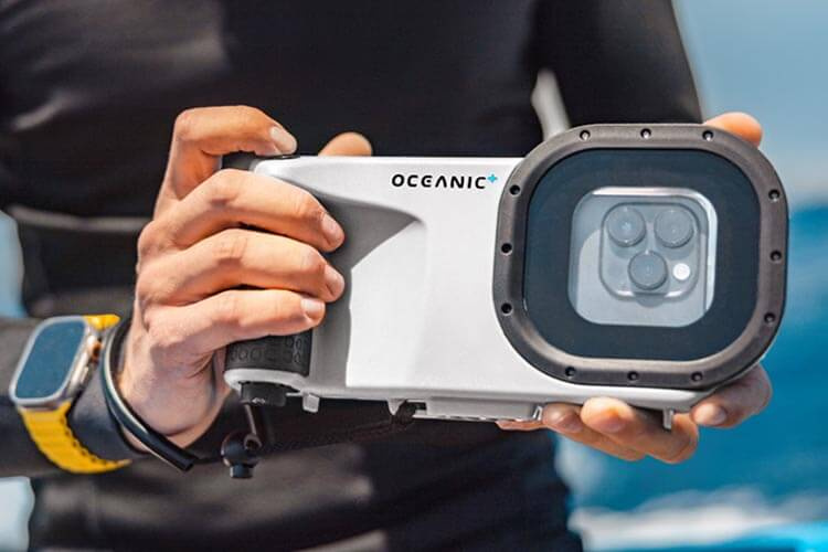 A person holding the Oceanic+ Dive Housing with an Apple Watch on a yellow band.