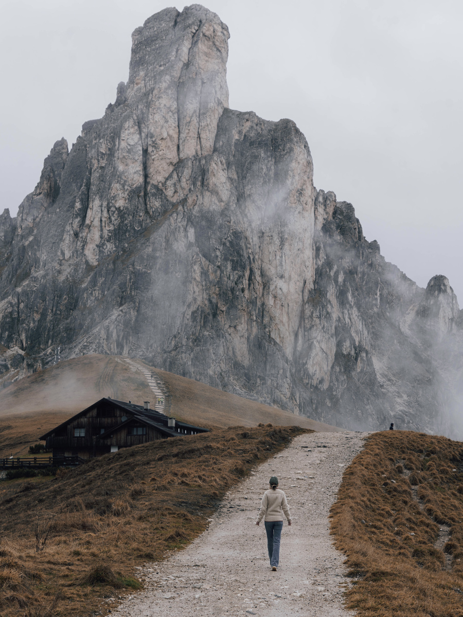 Olga walks towards a mountain hut beneath the cloud-wrapped rock tower of Ra Gusela.