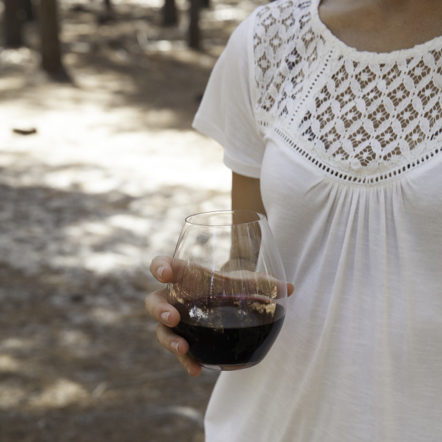 A hand holding a stemless glass of red wine outdoors.