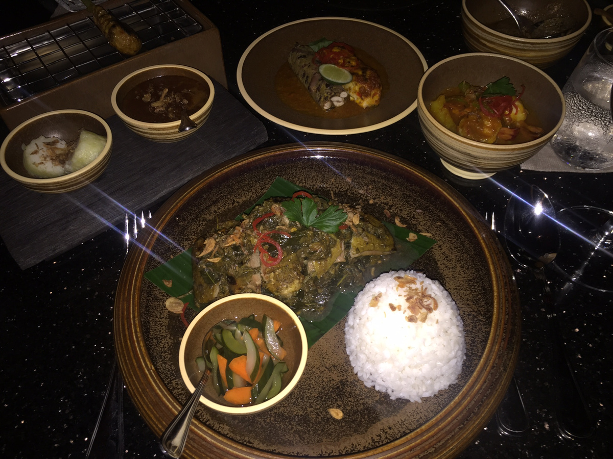 An Indonesian dinner of rice and several dishes served in bowls and on banana leaves