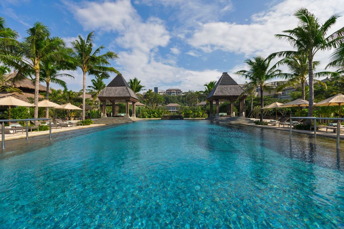 The outdoor swimming pool at The Ritz-Carlton, Bali, with shaded pavilions, palm trees and sun loungers