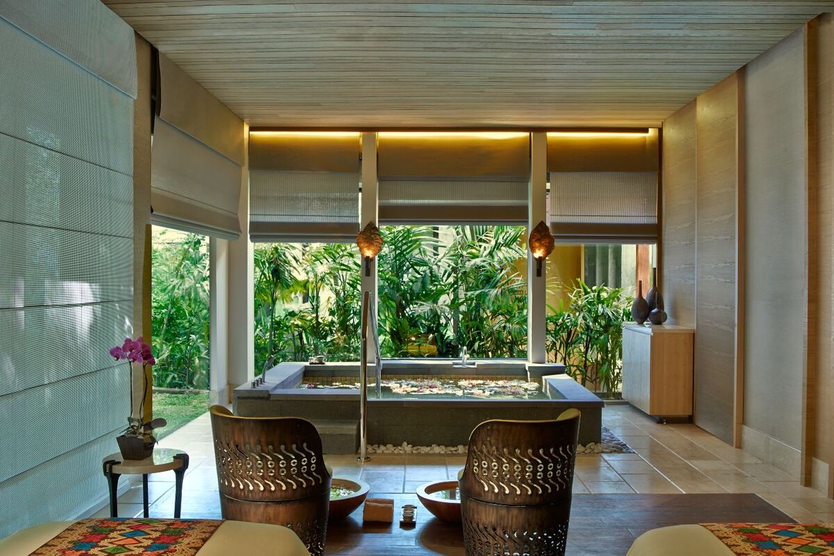 A spa villa at The Ritz-Carlton, Bali, with two chairs beside a flower-filled bath overlooking tropical planting