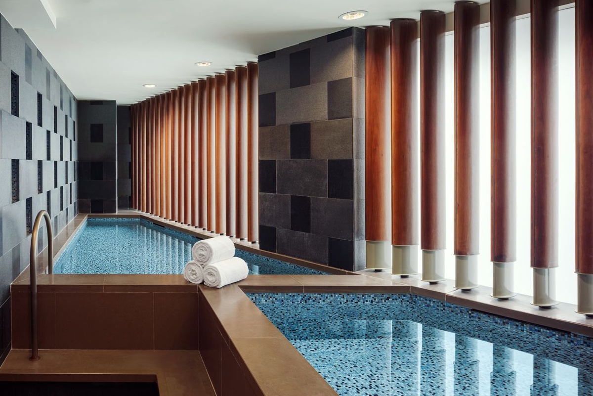 Mosaic-lined spa pools beside tall windows and wooden columns