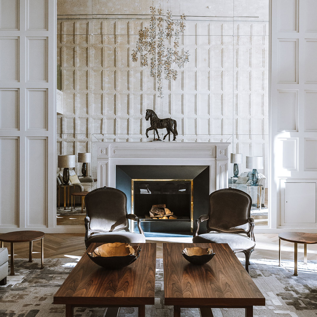 A white-panelled salon with a marble fireplace, two velvet armchairs, walnut tables and a bronze horse on the mantel.