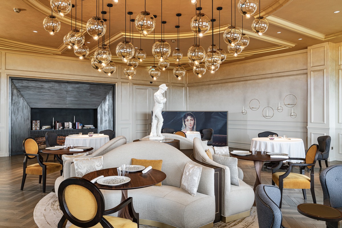 Le Royal dining room with round tables, glass pendant lights and a fireplace along the left wall.