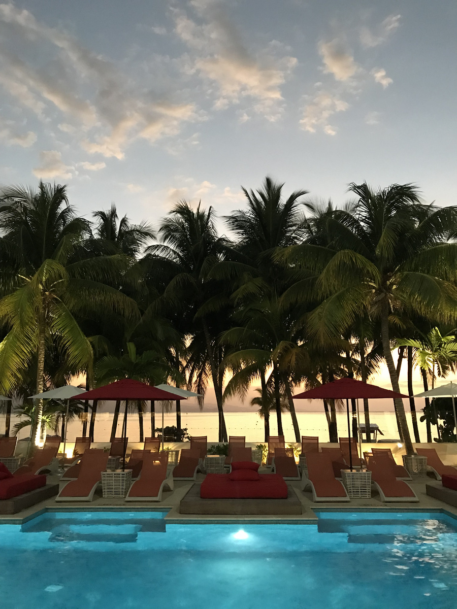Illuminated swimming pool beneath palms and red umbrellas at S Hotel Montego Bay.
