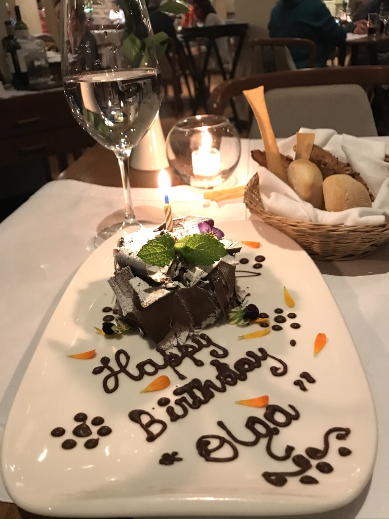 A small birthday cake with a candle sits on a plate bearing a birthday message for Olga.