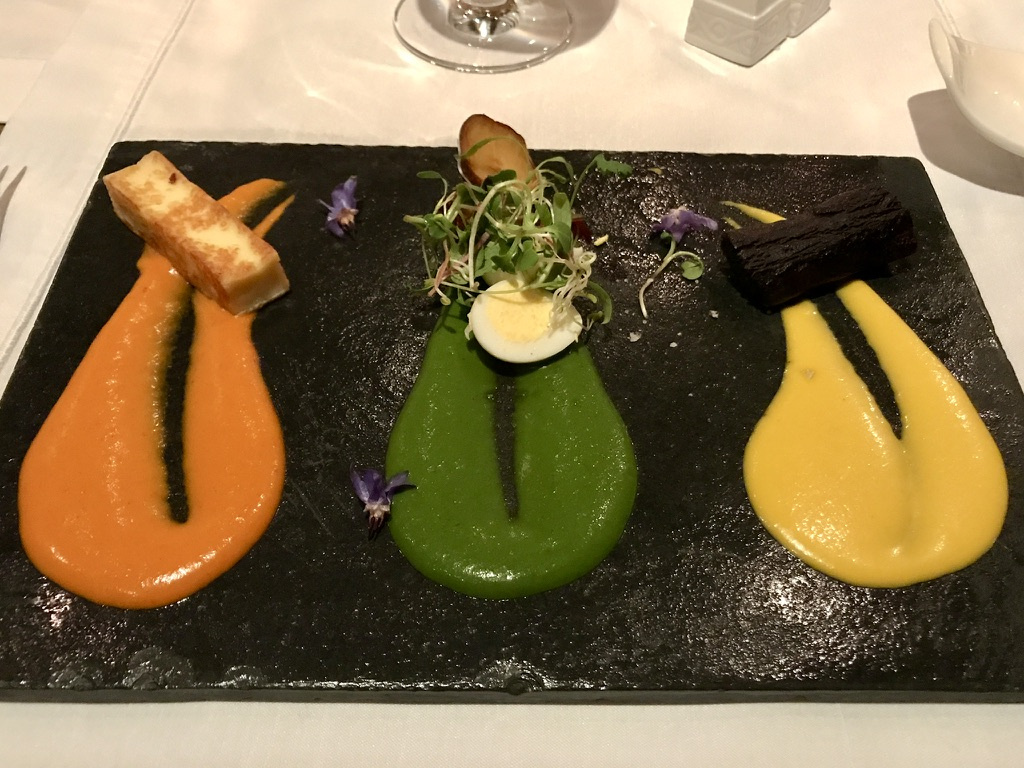 Three portions with orange, green, and yellow sauces are arranged on a dark rectangular serving plate.