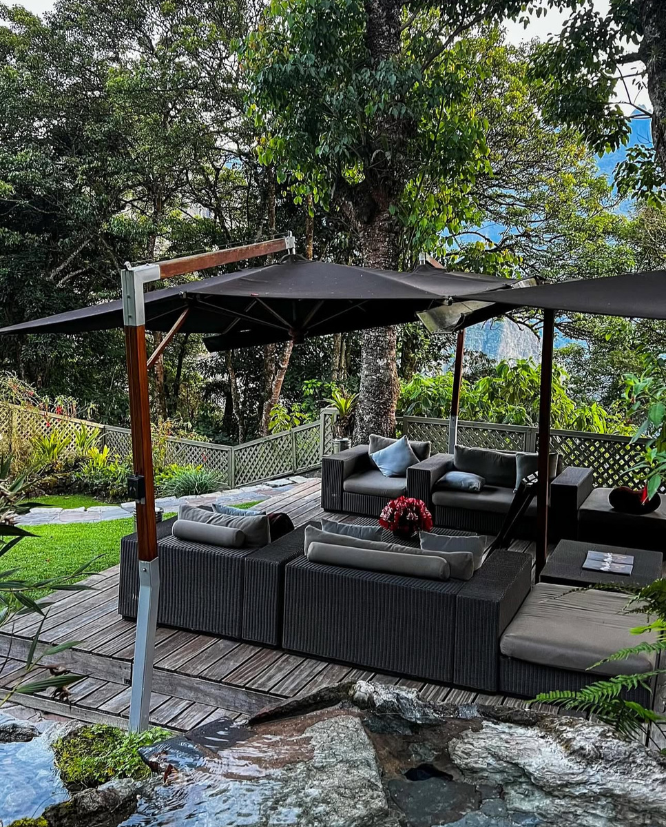Dark woven chairs sit beneath parasols on a wooden deck beside rocks and trees.