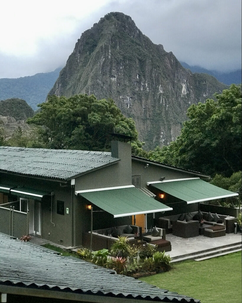 Huayna Picchu rises behind Sanctuary Lodge’s green roofs and an outdoor terrace.